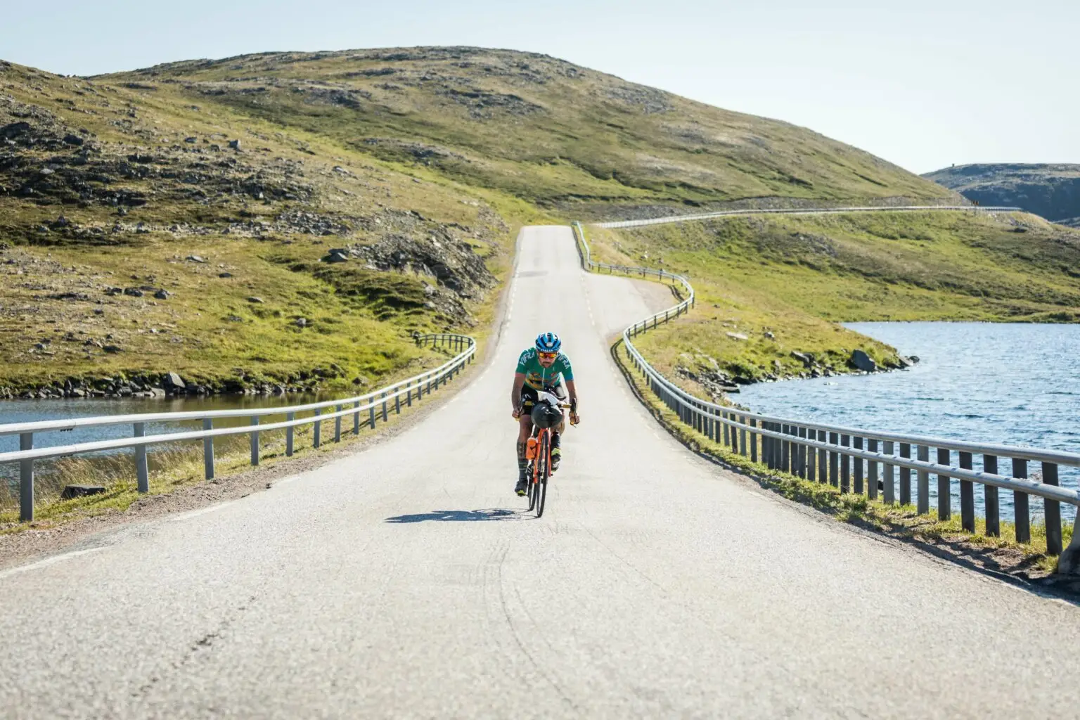 Ciclista in modalità bikepacking pedala su una strada panoramica del Nord Europa lungo un lago e colline